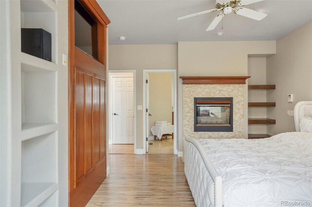 bedroom with ceiling fan, a multi sided fireplace, light hardwood / wood-style flooring, ensuite bathroom, and a closet