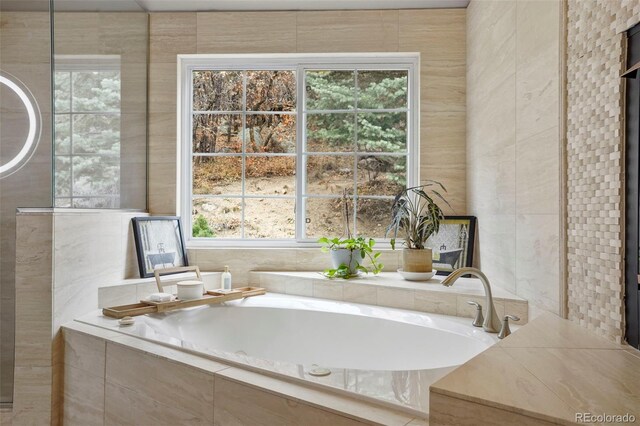 bathroom with tile walls, a relaxing tiled tub, and a healthy amount of sunlight