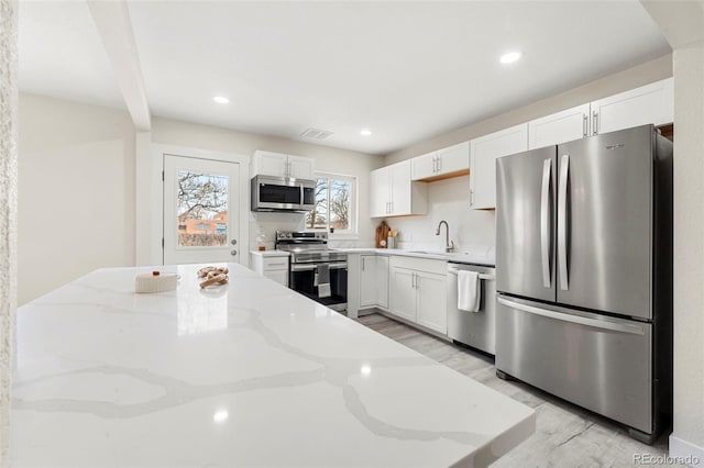 kitchen featuring white cabinets, appliances with stainless steel finishes, light stone counters, and sink