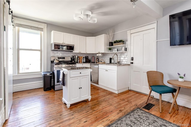 kitchen featuring dark stone counters, light hardwood / wood-style floors, a center island, white cabinets, and appliances with stainless steel finishes