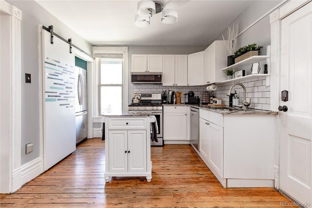 kitchen featuring white cabinets, stainless steel appliances, a barn door, and light hardwood / wood-style flooring