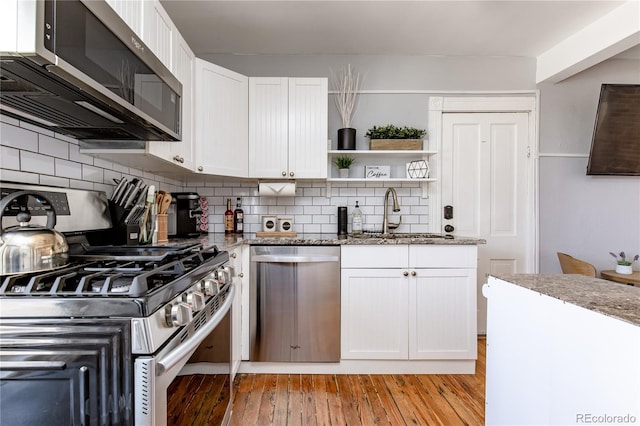 kitchen with appliances with stainless steel finishes, dark stone countertops, white cabinets, light wood-type flooring, and sink