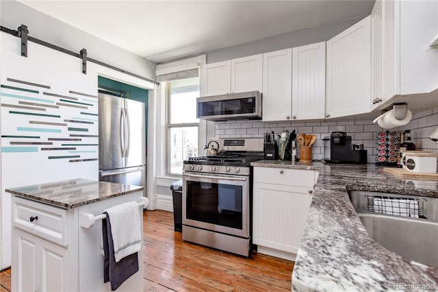 kitchen with white cabinets, stainless steel appliances, a barn door, dark stone countertops, and light hardwood / wood-style floors