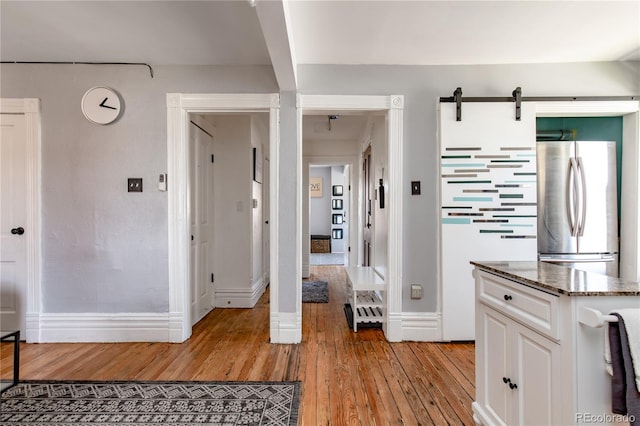 interior space featuring white cabinetry, a barn door, light hardwood / wood-style flooring, stainless steel refrigerator, and dark stone countertops