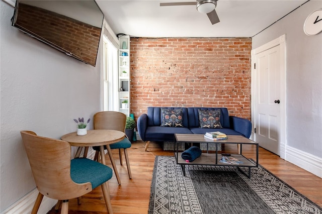 living room with ceiling fan, light wood-type flooring, and brick wall