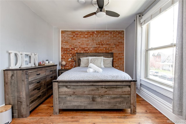 bedroom featuring light hardwood / wood-style flooring, ceiling fan, and brick wall