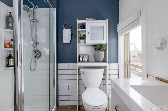 bathroom featuring tile walls, vanity, toilet, and a shower with shower door