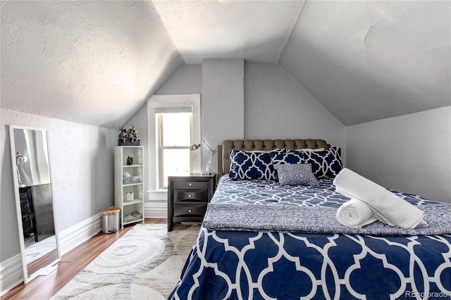 bedroom with lofted ceiling, a textured ceiling, and hardwood / wood-style flooring