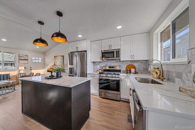 kitchen featuring vaulted ceiling, hanging light fixtures, appliances with stainless steel finishes, sink, and a center island