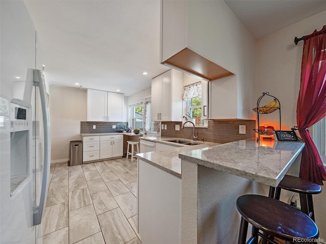 11399 Kendall St, Westminster, CO 80020 - kitchen with light stone countertops, freestanding refrigerator, white cabinetry, tasteful backsplash, and a peninsula