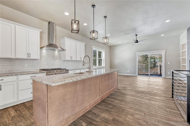 kitchen with pendant lighting, sink, white cabinets, a center island with sink, and wall chimney exhaust hood