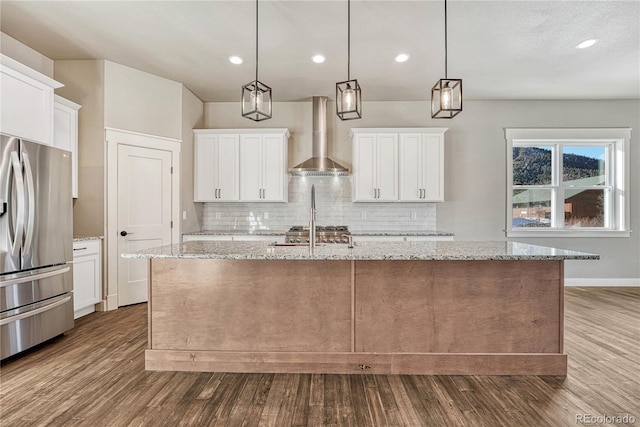 kitchen featuring wall chimney exhaust hood, appliances with stainless steel finishes, a kitchen island with sink, and pendant lighting