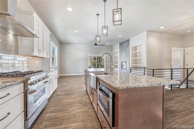 kitchen featuring stainless steel stove, white cabinets, pendant lighting, a kitchen island with sink, and wall chimney range hood