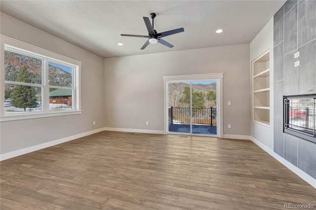 unfurnished living room with hardwood / wood-style flooring, ceiling fan, and built in shelves