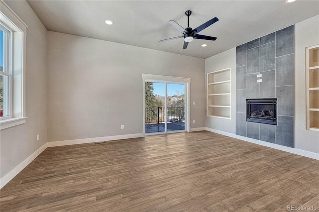 unfurnished living room featuring a tiled fireplace, hardwood / wood-style floors, built in features, and ceiling fan