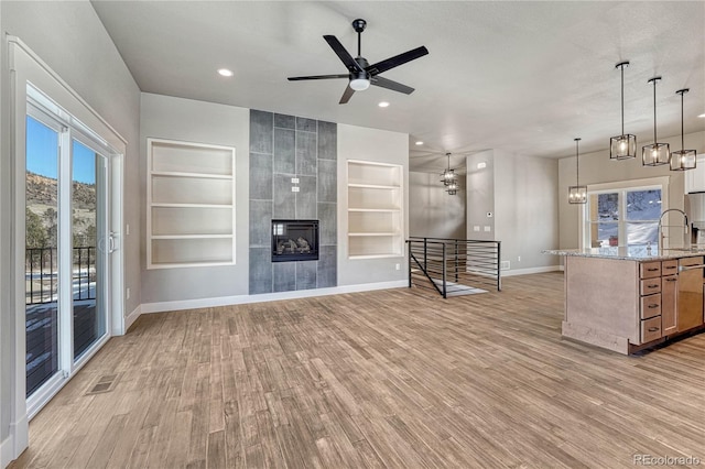 unfurnished living room with a tiled fireplace, sink, built in features, and light wood-type flooring