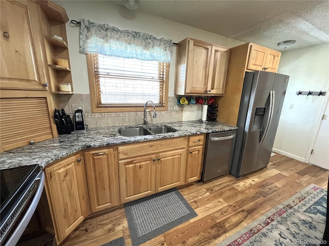 kitchen with stainless steel appliances, decorative backsplash, light wood-style floors, stone countertops, and a sink