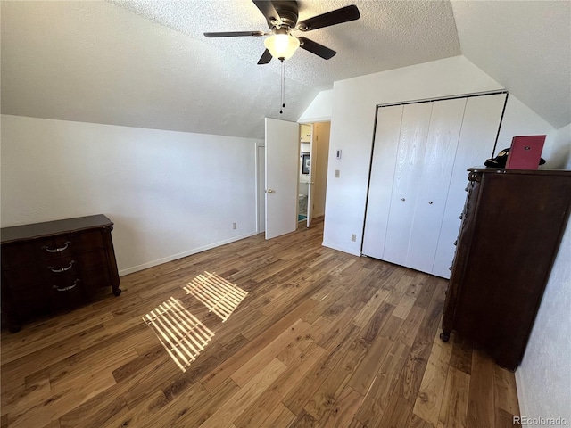 bedroom featuring a textured ceiling, lofted ceiling, wood finished floors, baseboards, and a closet