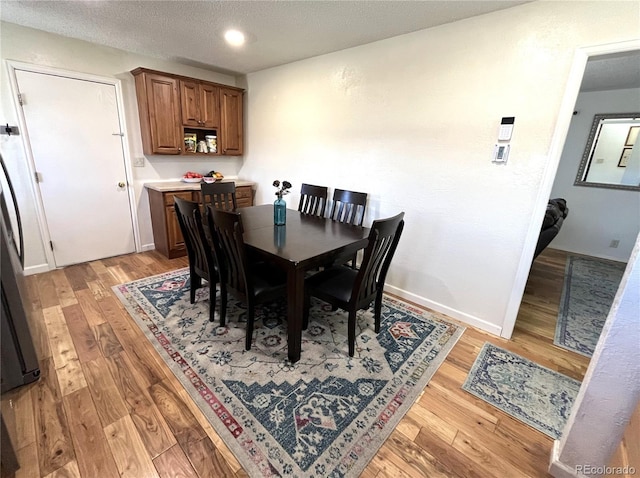 dining room with a textured ceiling, light wood finished floors, and baseboards