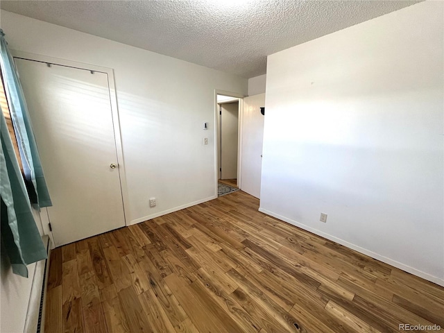 unfurnished bedroom with a textured ceiling, baseboards, and wood finished floors