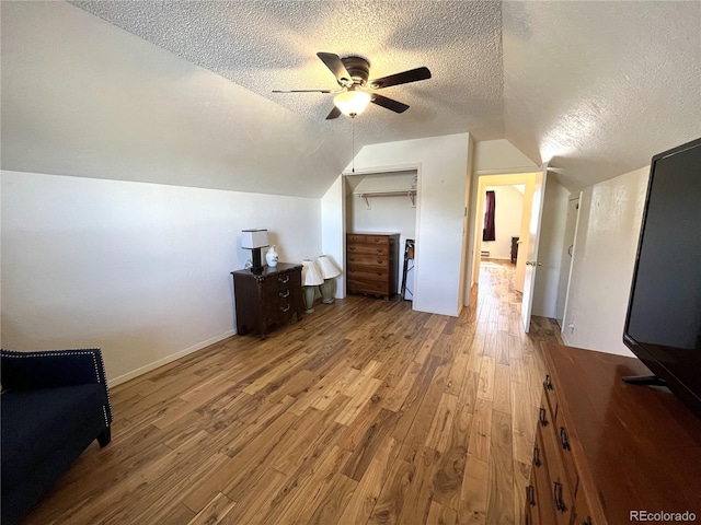 additional living space with lofted ceiling, a ceiling fan, a textured ceiling, wood finished floors, and baseboards