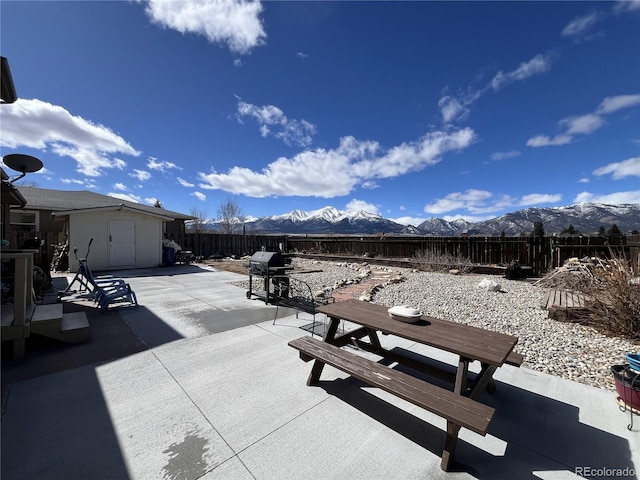 view of patio / terrace featuring outdoor dining area, a fenced backyard, a mountain view, and an outdoor structure