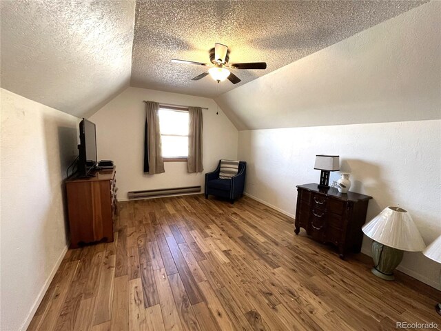 additional living space featuring a textured ceiling, a baseboard radiator, hardwood / wood-style flooring, a ceiling fan, and vaulted ceiling