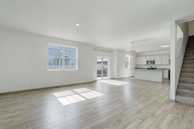 unfurnished living room featuring stairs, recessed lighting, baseboards, and light wood finished floors