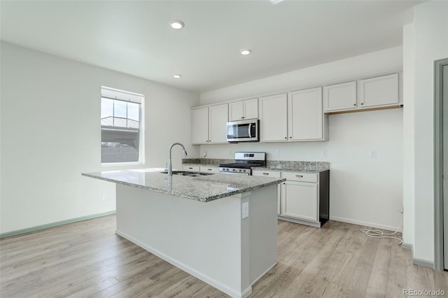 kitchen featuring light wood finished floors, light stone countertops, a center island with sink, stainless steel appliances, and a sink