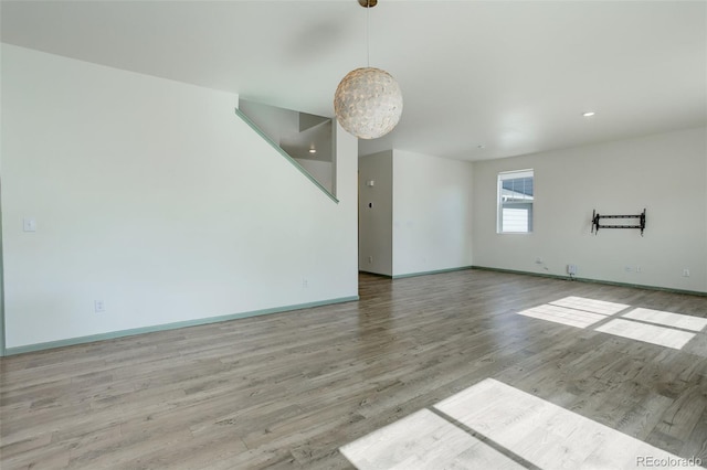 spare room with an inviting chandelier, baseboards, and wood finished floors