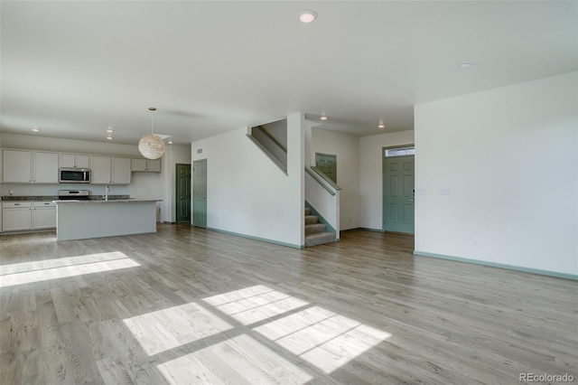 unfurnished living room with light wood finished floors, recessed lighting, stairs, and baseboards