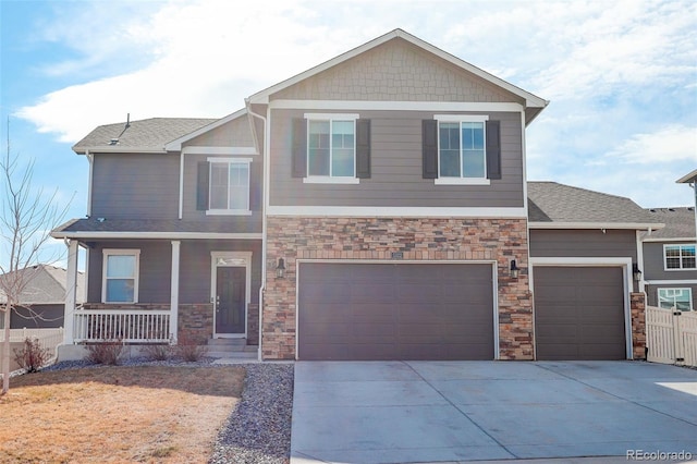 craftsman-style house featuring stone siding, covered porch, concrete driveway, and fence