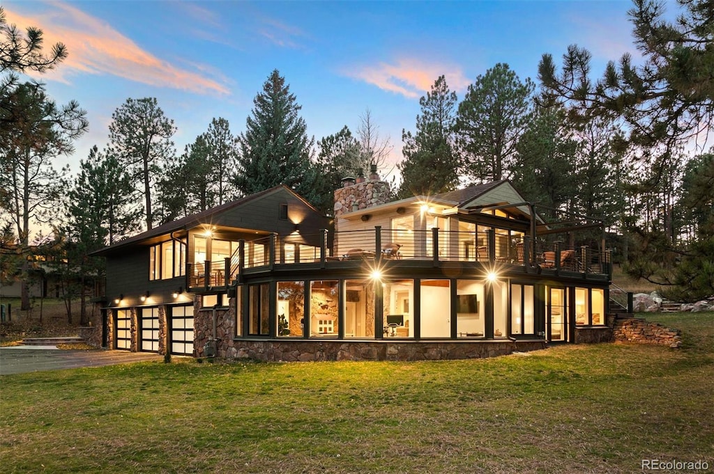 back house at dusk featuring a yard, a balcony, and a garage