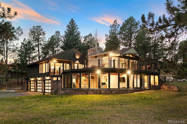 back house at dusk featuring a yard, a balcony, and a garage