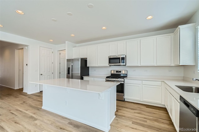 kitchen with a center island, light wood-type flooring, appliances with stainless steel finishes, white cabinetry, and a sink