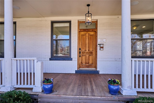 view of exterior entry with brick siding and a porch