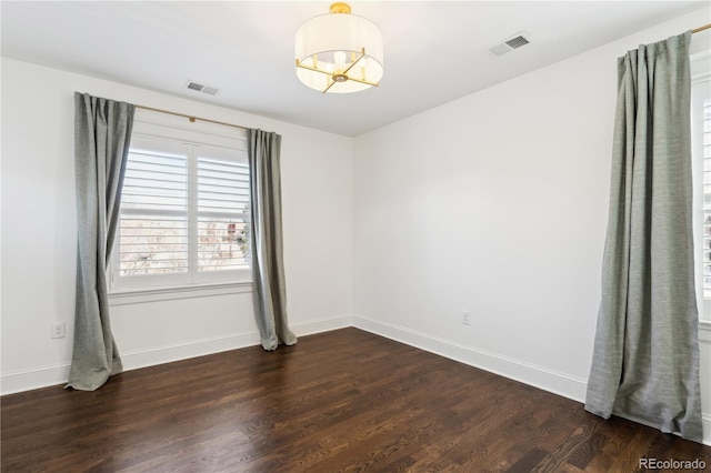 empty room featuring visible vents, baseboards, dark wood-type flooring, and a chandelier