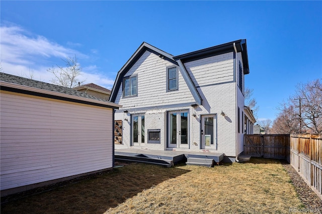 back of house featuring brick siding, a wooden deck, a lawn, a fenced backyard, and a gate