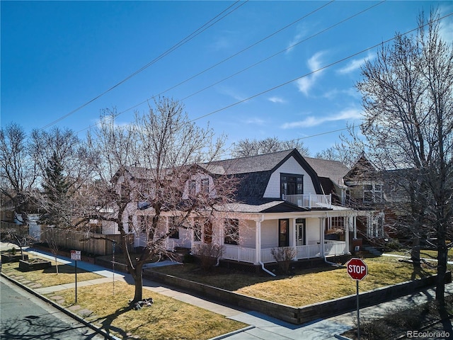 dutch colonial featuring a gambrel roof, a porch, a front yard, a shingled roof, and a balcony