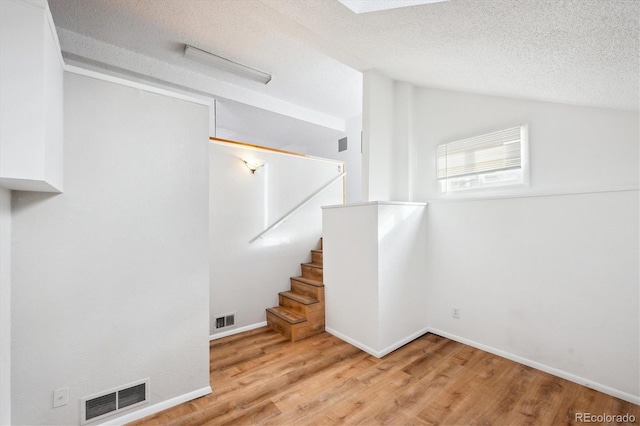 stairs with lofted ceiling, hardwood / wood-style flooring, and a textured ceiling