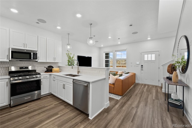 kitchen featuring decorative backsplash, appliances with stainless steel finishes, a sink, a peninsula, and open floor plan
