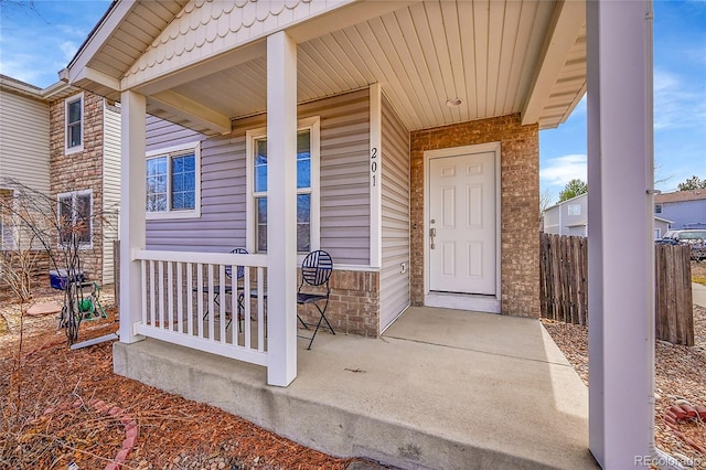 entrance to property with stone siding, covered porch, brick siding, and fence