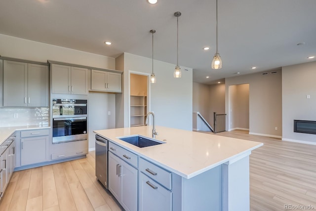 kitchen featuring pendant lighting, sink, gray cabinets, stainless steel appliances, and a center island with sink