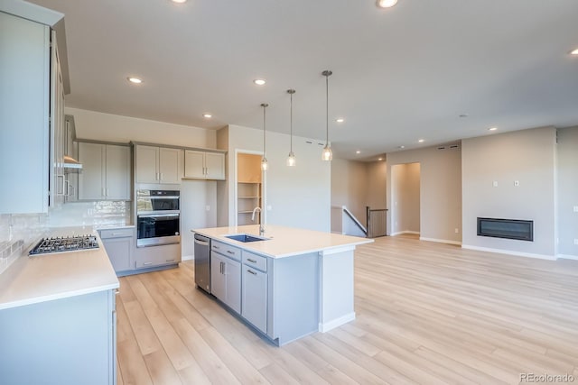 kitchen featuring sink, decorative light fixtures, light wood-type flooring, appliances with stainless steel finishes, and an island with sink