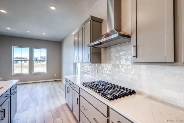 kitchen featuring wall chimney range hood, gray cabinets, decorative backsplash, stainless steel gas stovetop, and light wood-type flooring