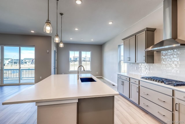 kitchen featuring wall chimney exhaust hood, sink, stainless steel gas stovetop, a kitchen island with sink, and backsplash