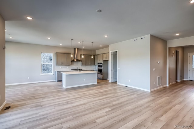 kitchen featuring sink, hanging light fixtures, a center island with sink, gray cabinets, and stainless steel double oven