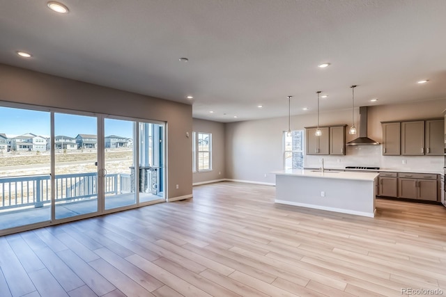 kitchen featuring sink, hanging light fixtures, a kitchen island with sink, wall chimney exhaust hood, and light hardwood / wood-style flooring