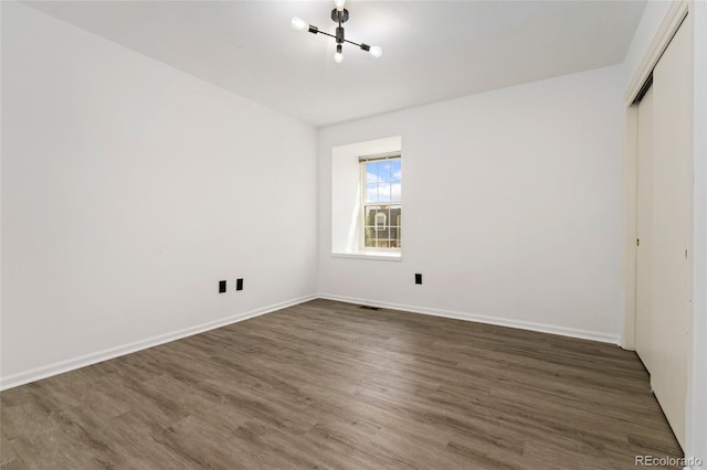 unfurnished bedroom featuring a chandelier, dark wood-style floors, a closet, and baseboards