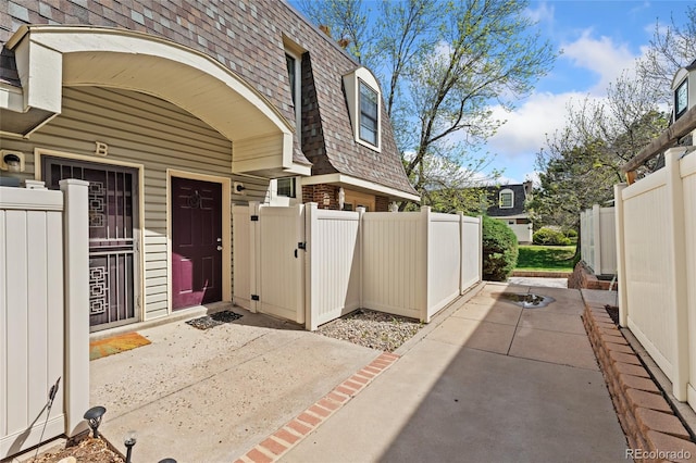 doorway to property featuring mansard roof, a gate, a shingled roof, and fence